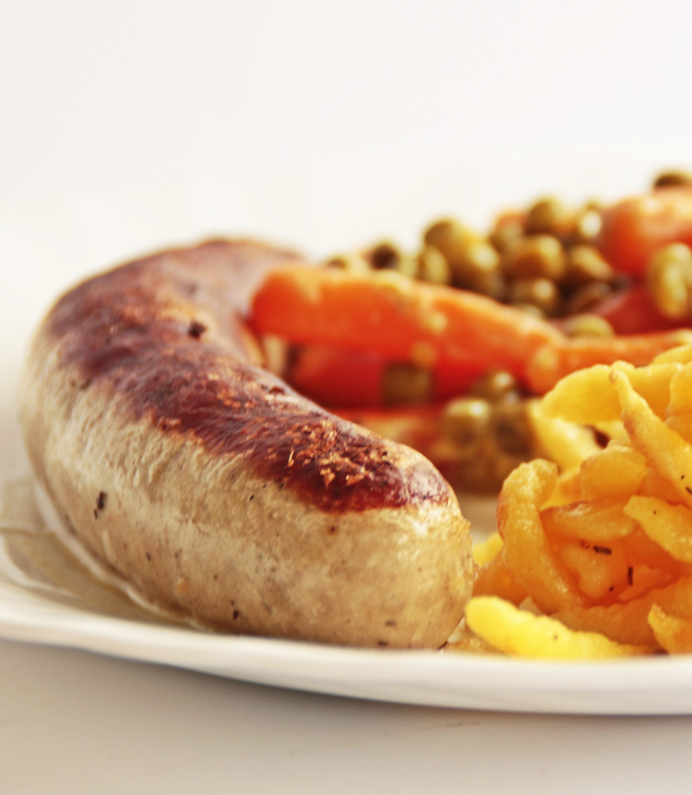 A German Bratwurst on a plate with chips and veggies