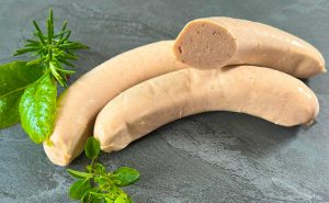 Raw German Bratwurst sausages on a stone surface with fresh herbs