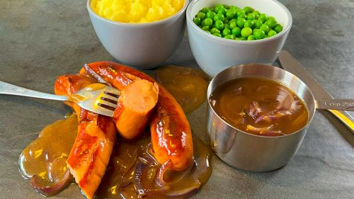 Cheese Frankfurter sliced and served with rich onion gravy, mashed potatoes, and peas — a hearty wholesale serving idea for caterers and pubs.