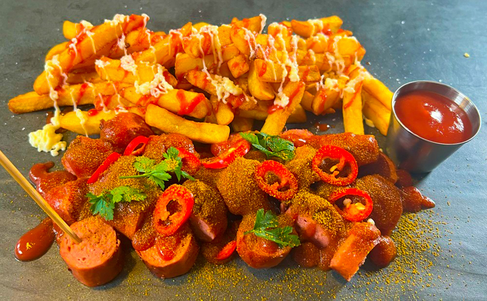 Chilli Frankfurter currywurst topped with sliced red chillies and curry powder, served with fries, ketchup, and mayonnaise — authentic German sausages wholesale UK.
