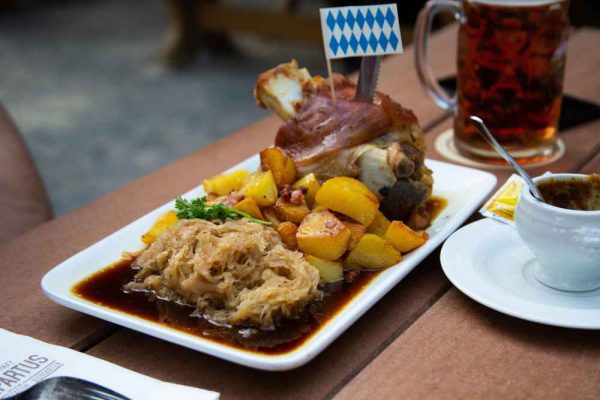 Traditional Bavarian meal featuring bratkartoffeln potatoes, sauerkraut, and roasted pork knuckle — a classic example of German comfort food often served with sausages and beer