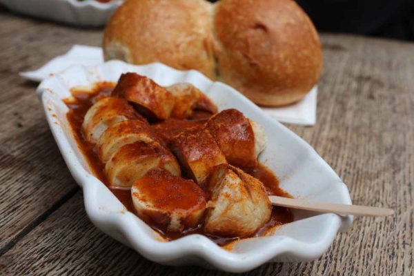 Authentic German currywurst in a white tray served with curry ketchup sauce and bread rolls — a classic Berlin street food loved across Germany and the UK