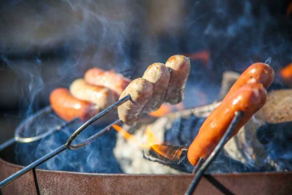 Bratwurst and Frankfurter sausages grilling over open fire – authentic German sausages cooked outdoors.