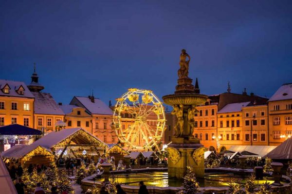 A festive Christmas market at dusk with food stalls, a ferris wheel, and a glowing fountain — the perfect setting for serving authentic German sausages and hot winter BBQ dishes.