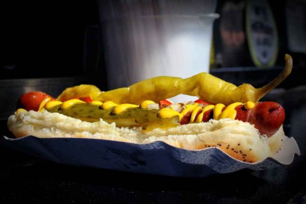 Hot dog in a bun with mustard, pickles, and pepper showing the difference between a hot dog and a frankfurter.