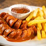 German currywurst with fries and currywurst sauce — sliced bratwurst covered in rich curry ketchup served with golden chips, the authentic German street food classic