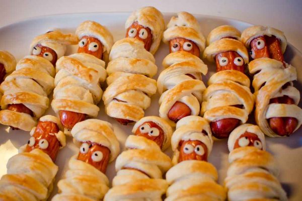Mummy-style hotdogs wrapped in golden puff pastry with candy eyes — a fun Halloween sausage for pubs, caterers, and events.