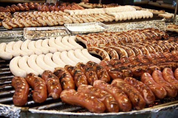 Rows of authentic German sausages sizzling on a large grill at a funfair or Oktoberfest event.
