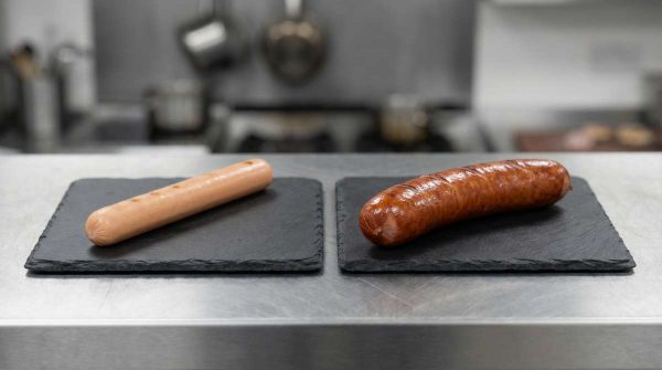 Side-by-side trade comparison: a generic thin skinless frankfurter versus the thicker smoked Sausage Haus Bacon Frankfurter (Bacon Krakauer style) for UK buyers.