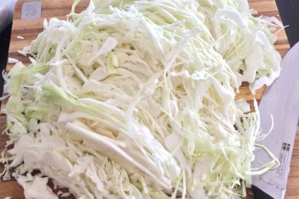 Freshly shredded white cabbage on a wooden board ready for fermentation — first step in making authentic German sauerkraut