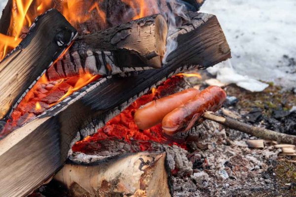 German sausages being grilled over glowing bonfire embers, showing how to cook Bratwurst, Krakauer, or Käsekrainer (Cheese Frankfurter) over an open fire.