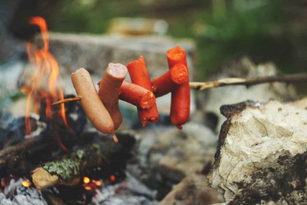German sausages being grilled over an open fire on sticks, showing the traditional way to cook Bratwurst and Cheese Frankfurter for Bonfire Night.
