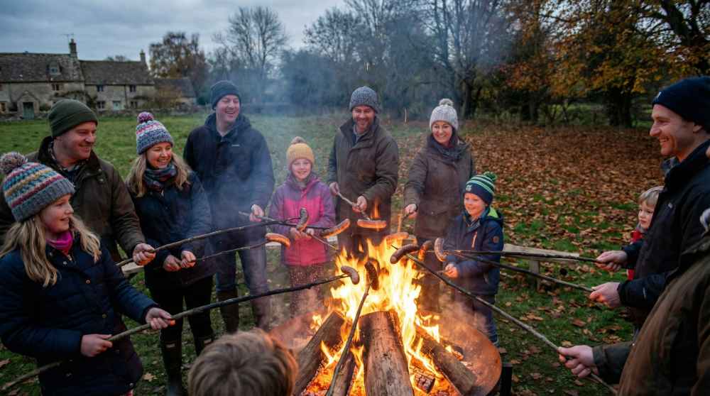 How to grill german sausages over an open fire, with people roasting sausages on sticks outdoors