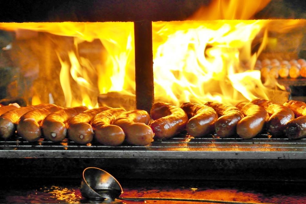 Smoked German sausages grilling over open flames on a hot BBQ grill