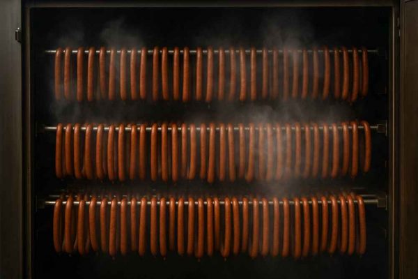 Hundreds of real German Frankfurters hanging in an industrial smoker, gently cooking over natural smoke to develop authentic flavour.