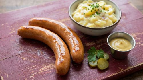 German Bockwurst sausages served with Southern German potato salad, mustard and pickles on a rustic wooden board