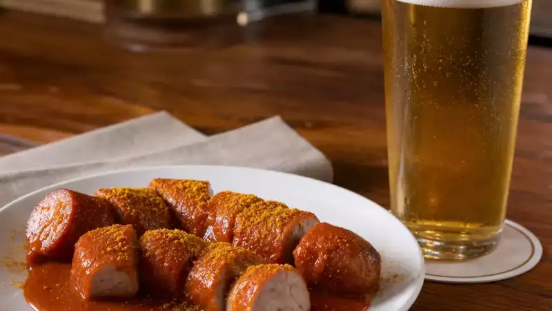 Currywurst-style sausage with curry ketchup served beside a chilled lager, suggesting a simple pub pairing that is easy to explain and sell.