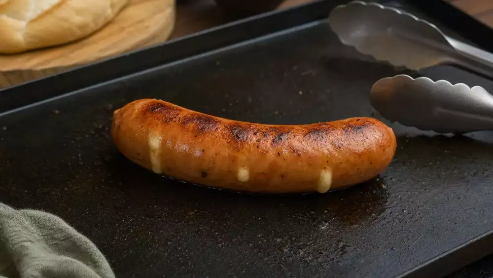 A Käsekrainer sausage gently browning on a grill with a little cheese just starting to seep out.