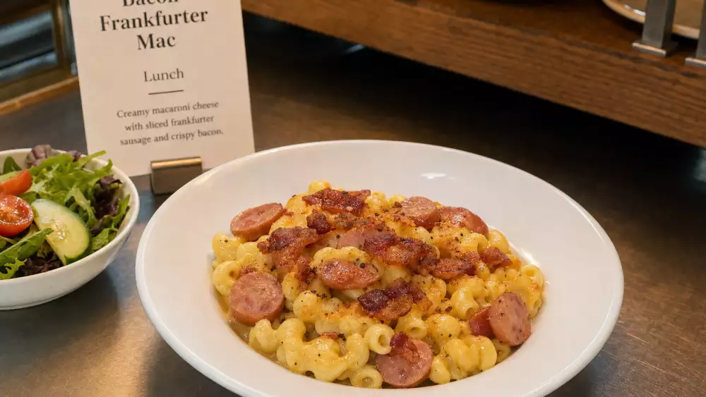 A café-style plated portion of bacon frankfurter mac and cheese with a small lunch menu card.